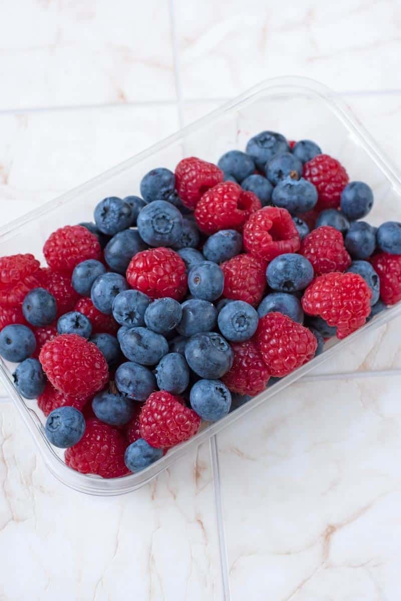 A plastic container full of blueberries and raspberries.