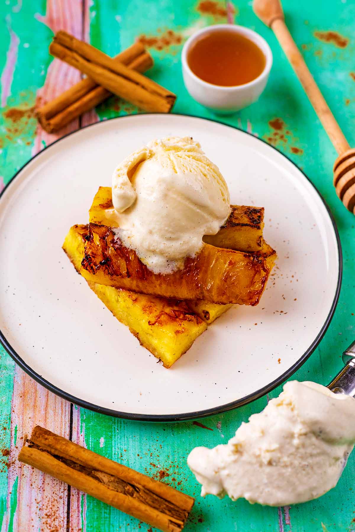 Grilled fingers of pineapple on a plate with a ball of vanilla ice cream.