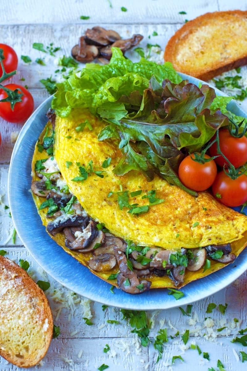 Mushroom omelette and salad on a plate with bread and tomatoes.
