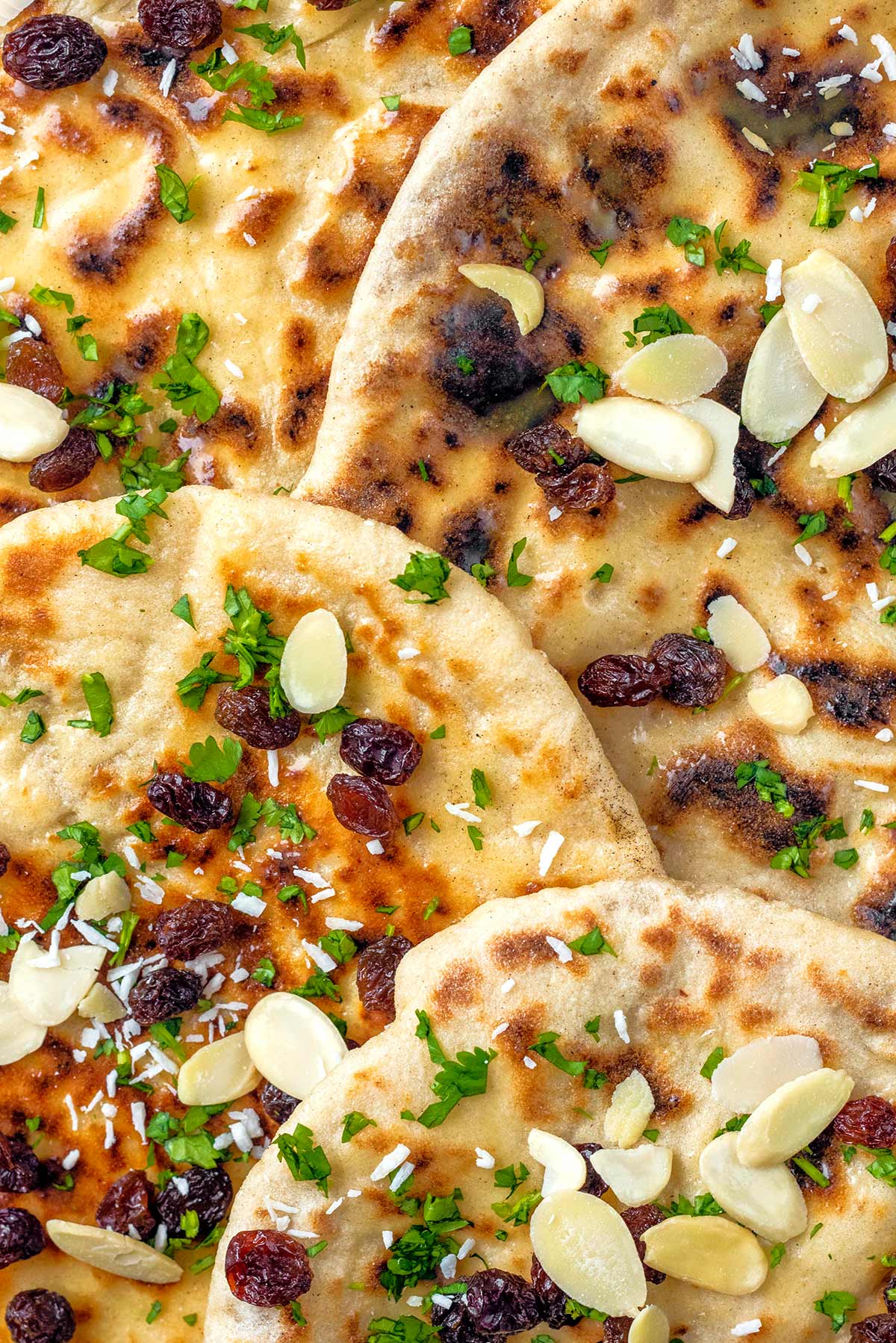 Naan breads on top of each other topped with raisins, flaked almonds and chopped coriander leaves.