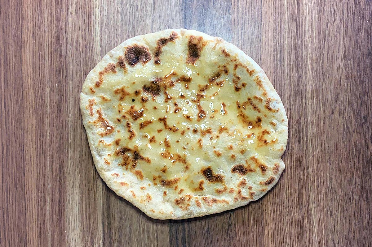 A cooked naan bread brushed with melted butter.
