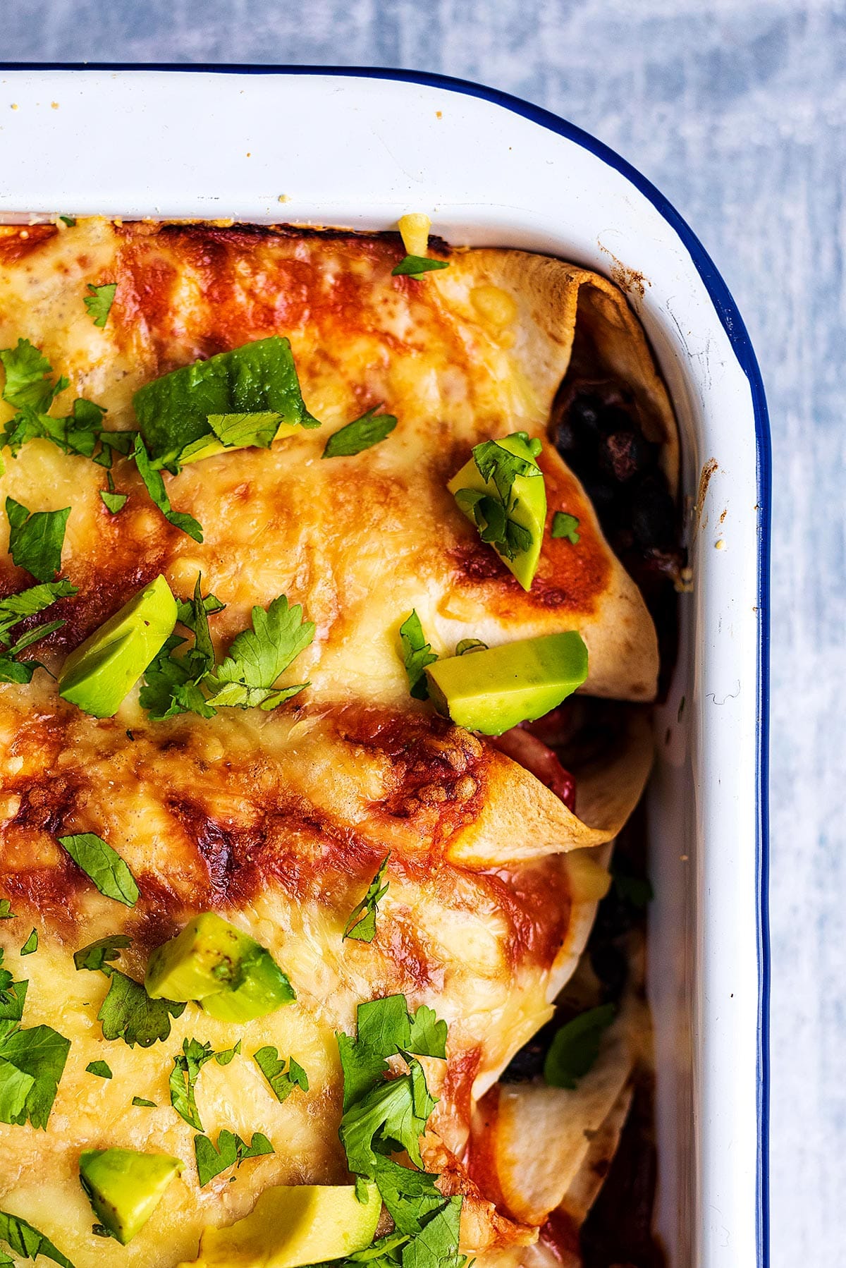 The corner of a baking dich containing cooked enchiladas.