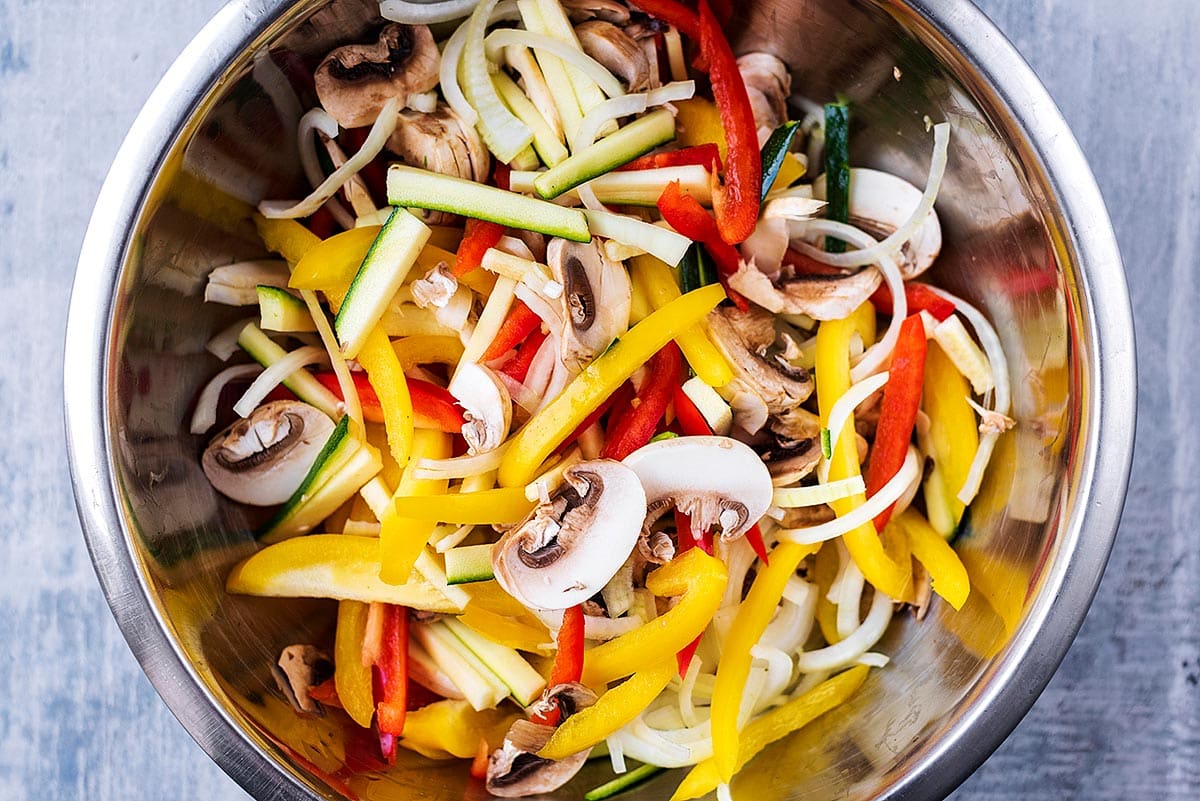 A large metal bowl full of sliced vegetables.