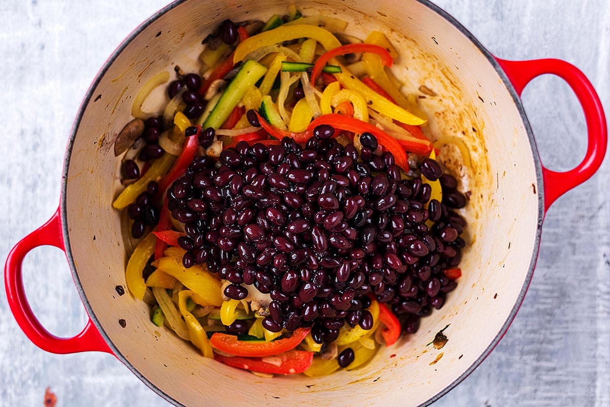 A large cooking pot with sliced vegetables and black beans cooking in it.