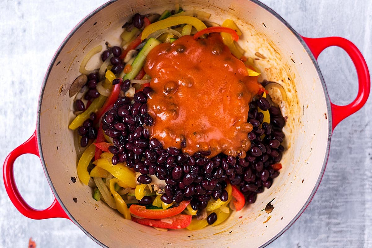 Black beans, sliced peppers and enchilada sauce cooking in a pan.