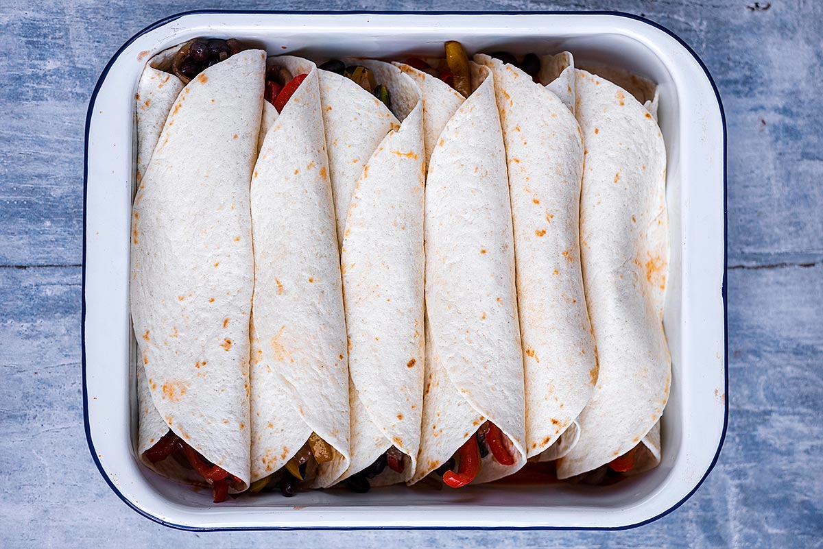 A baking dish with six uncooked enchiladas in it.