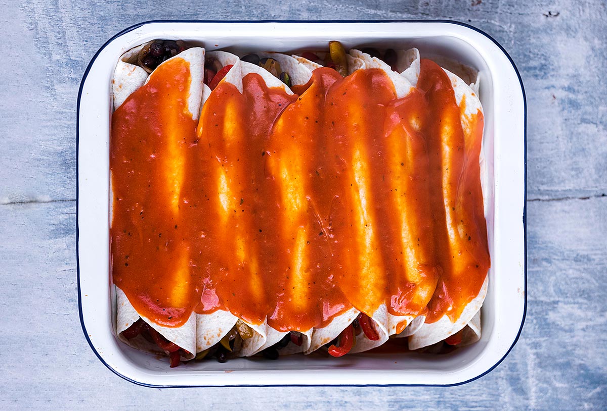 Enchiladas in a baking dish smothered with sauce.