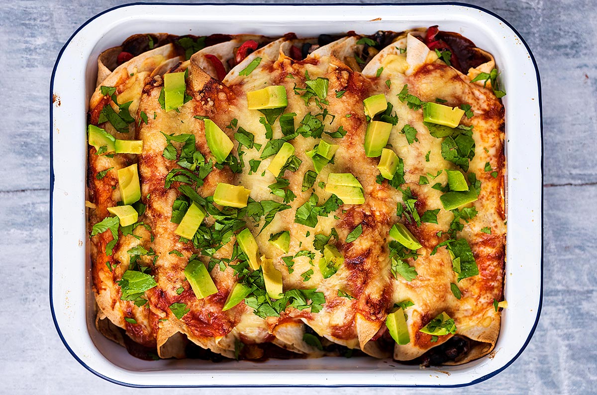 Cooked enchiladas topped with herbs and avocado cubes.