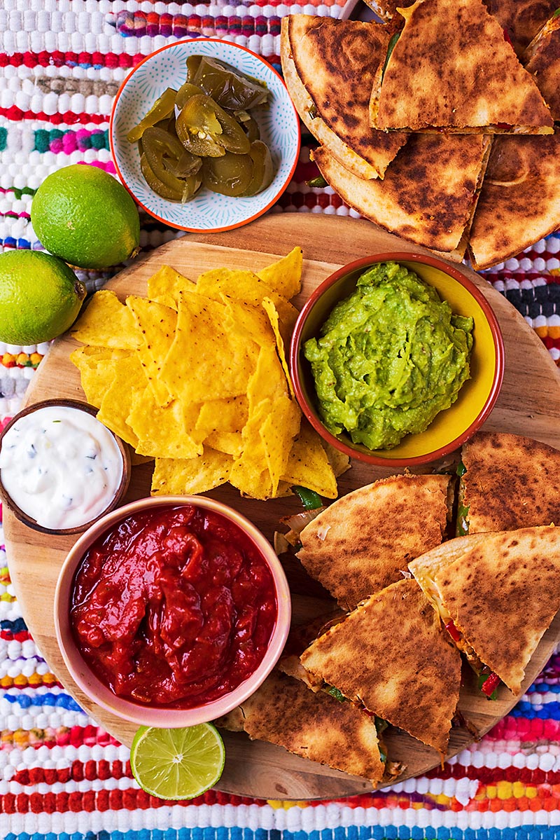 Chicken Quesadillas set out with tortilla chips, dips, pickled jalapenos and lime wedges