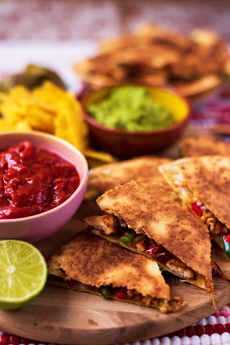Quesadillas on a board with chips and dips in the background