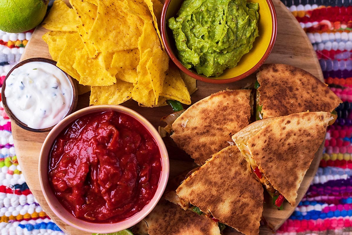 A board full of quesadillas on a colourful table cloth