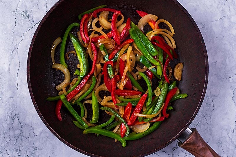 Sliced peppers and onions cooking in a frying pan