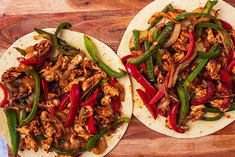 Two flour tortillas covered in cooked and seasoned chicken and vegetables