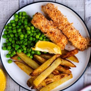 Homemade Fish Fingers on a plate with chips, peas and a lemon wedge