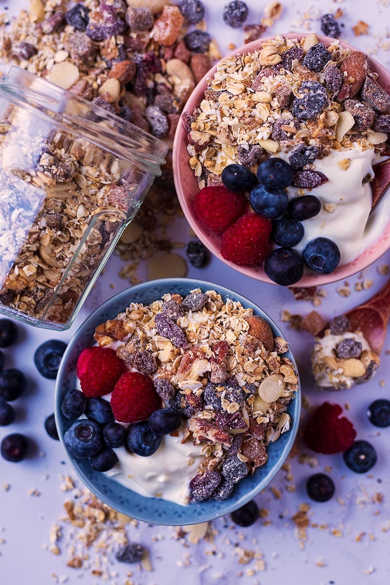 Two bowls of yogurt topped with muesli and berries.