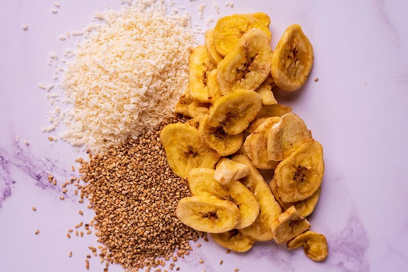 Dried banana slices, desiccated coconut and flax seeds on a marble surface.