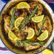 Lemon and herb chicken in a large round pan topped with lemon slices and rosemary sprigs.