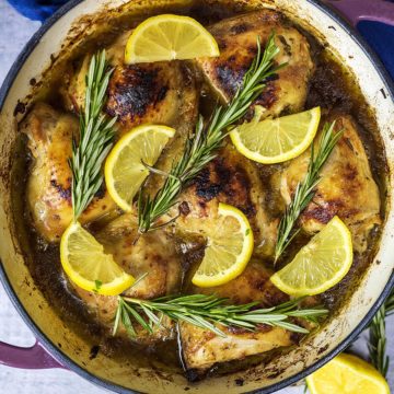 Lemon herb chicken in a round pan topped with lemon slices and rosemary sprigs.