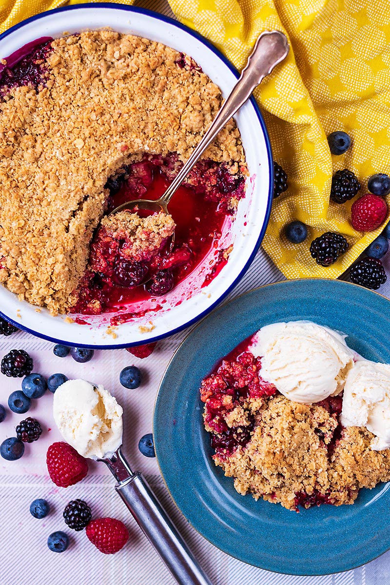 Mixed Berry Crisp in a bowl with icecream next to a baking dish of more berry crisp