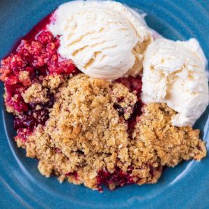 Mixed Berry Crisp in a blue bowl with two balls of vanilla ice cream