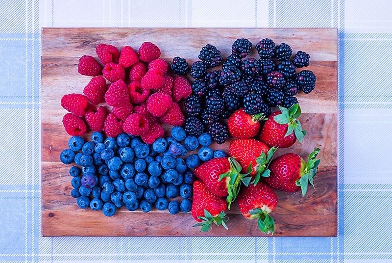 A wooden board covered in raspberries, blackberries, blueberries and strawberries