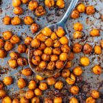 A spoonful of roasted chickpeas on a baking tray with more chickpeas.
