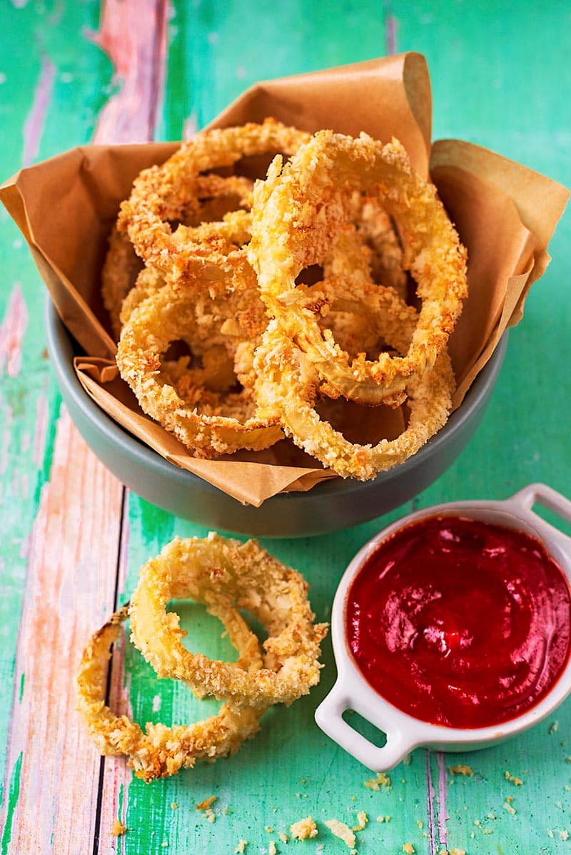 Baked onion rings in a lined dish with a pot of tomato ketchup.
