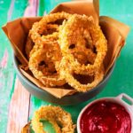 A bowl of baked onion rings next to a small pot of ketchup