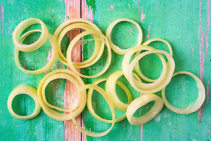 An onion cut into rings on a green wooden surface.