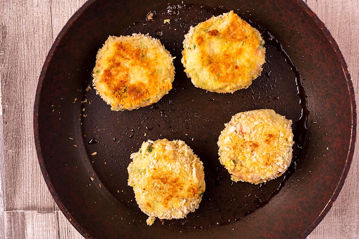 A frying pan with four fishcakes cooking in it.