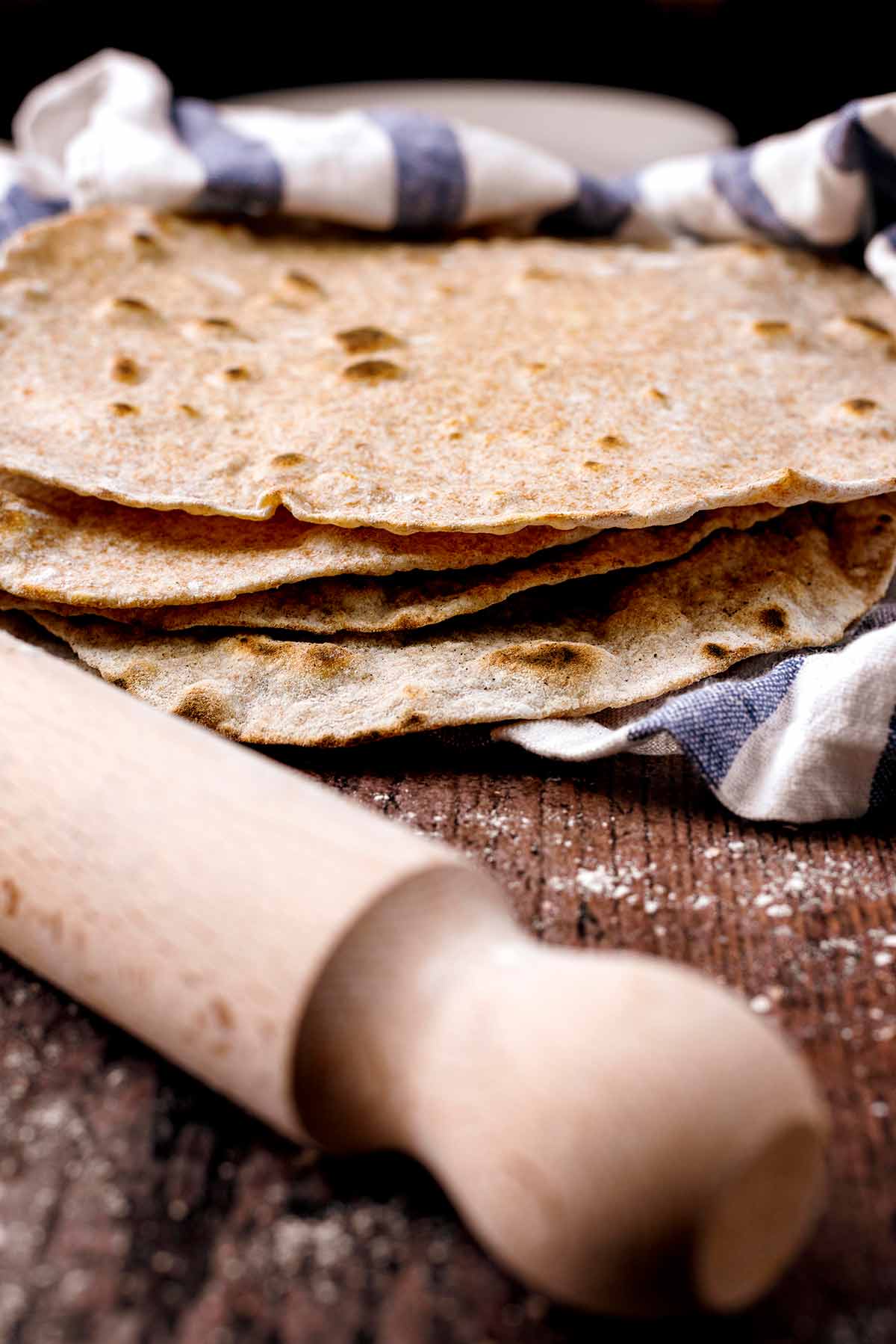 A pile of tortilla wraps with a rolling pin in the foreground.