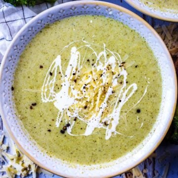 Cauliflower and broccoli soup in a bowl with cream, cheese and black pepper on top.