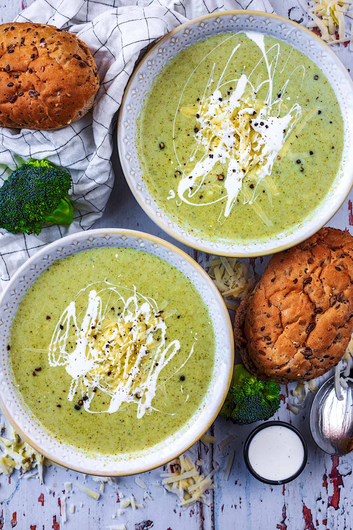Two bowls of soup with two bread rolls next to them.