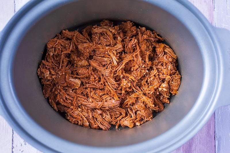 A slow cooker pot containing shredded pork