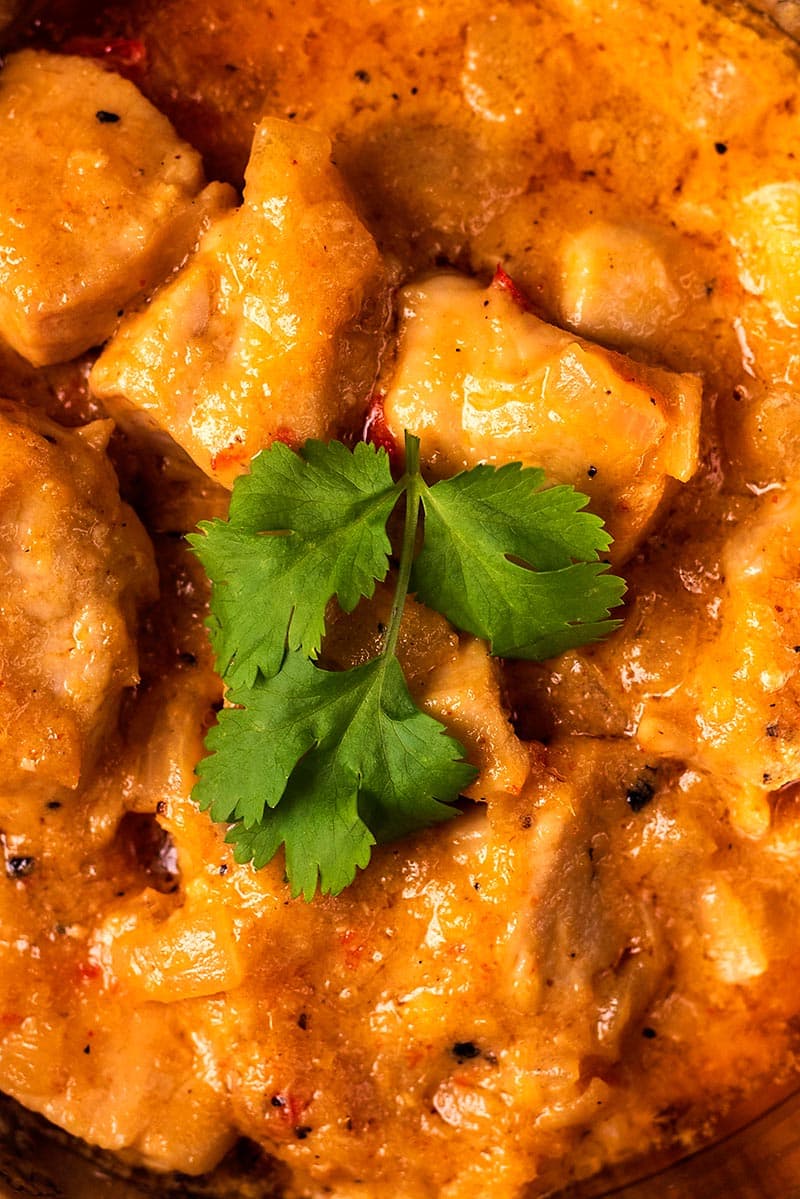 Chunks of chicken in a curry sauce topped with a cilantro leaf.