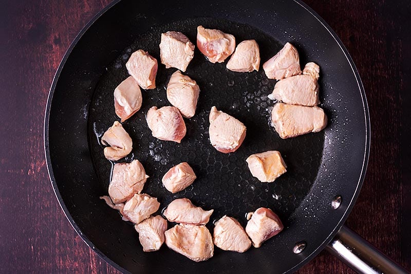 Chunks of chicken breast frying in a pan.
