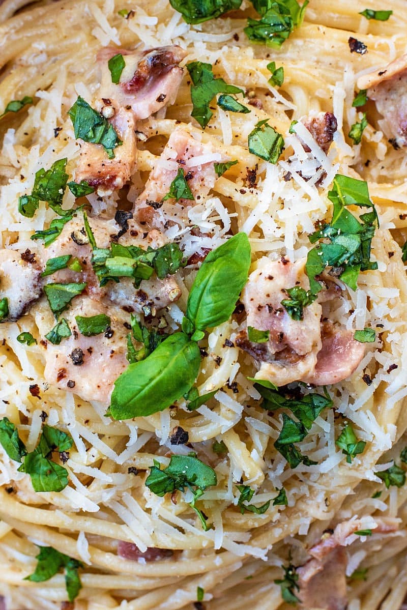 Basil leaves on top of a dish of pasta carbonara.