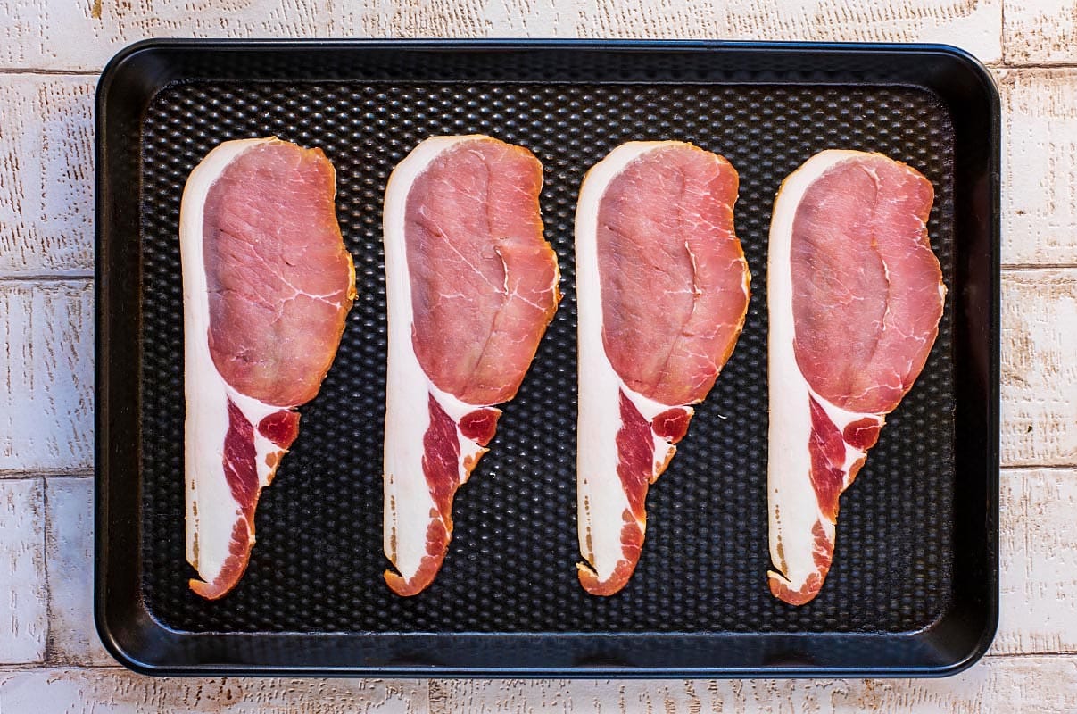 A black baking tray with four rashers of bacon.