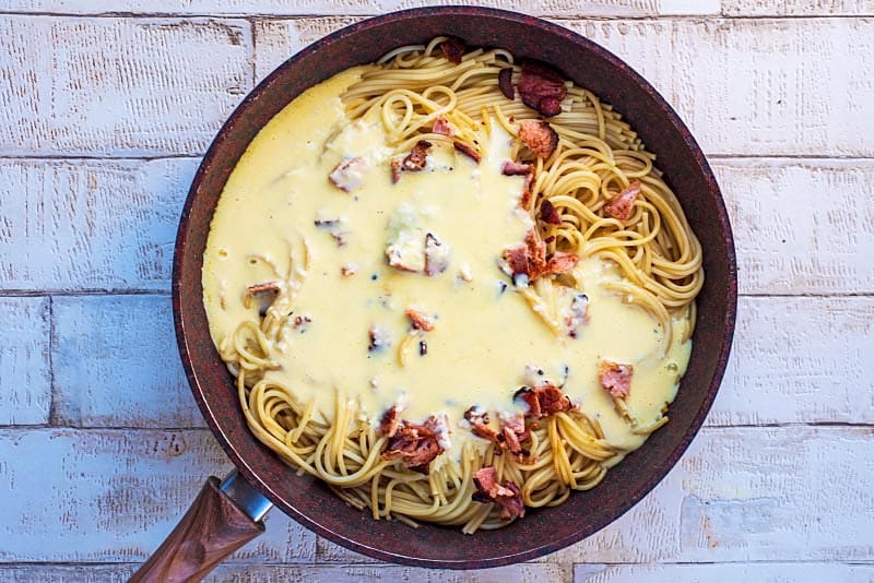 A frying pan containing spaghetti in a creamy sauce.