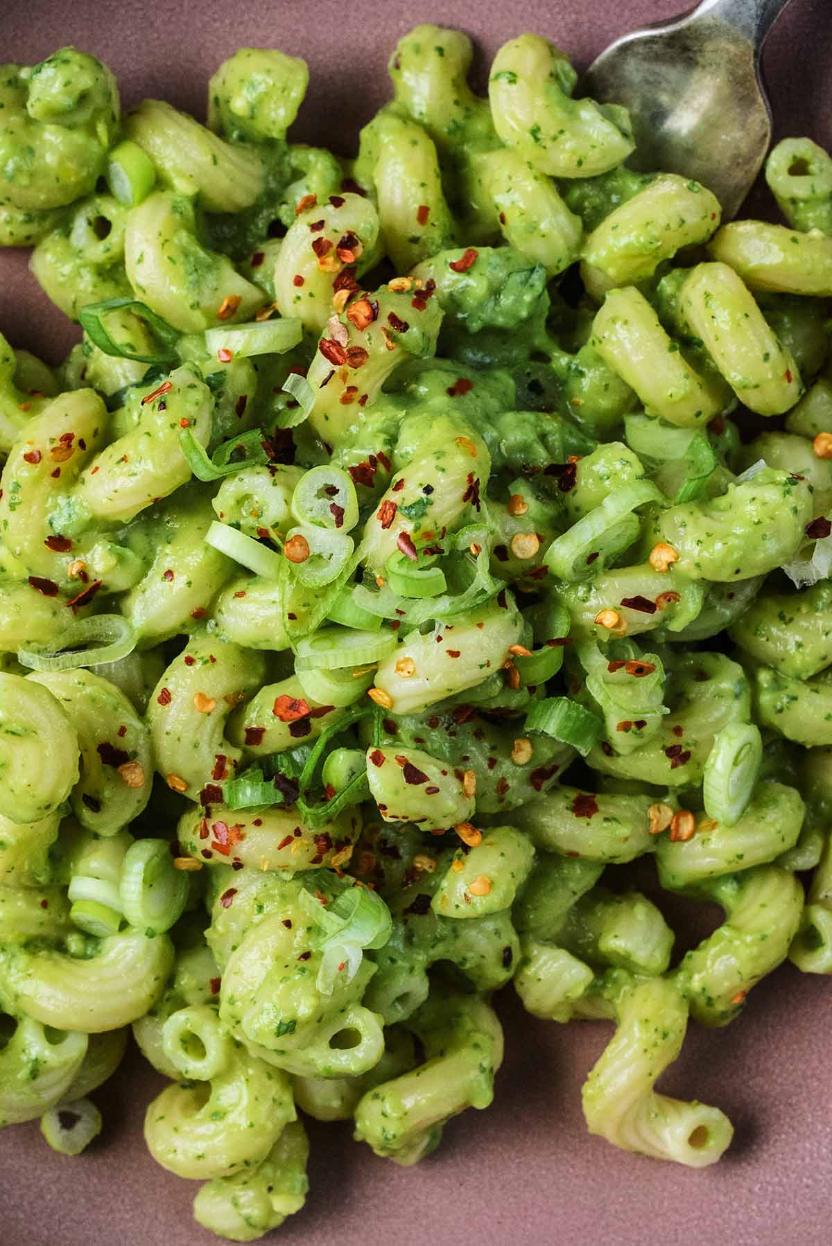 Pasta spirals in a green sauce with sliced onion and chilli flakes.