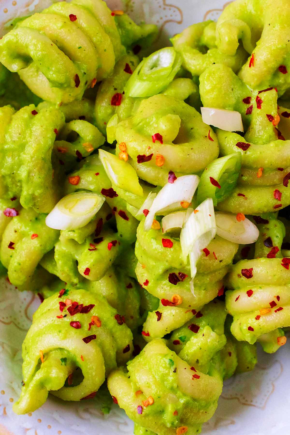 Pasta spirals in a green sauce with sliced onion and chilli flakes.