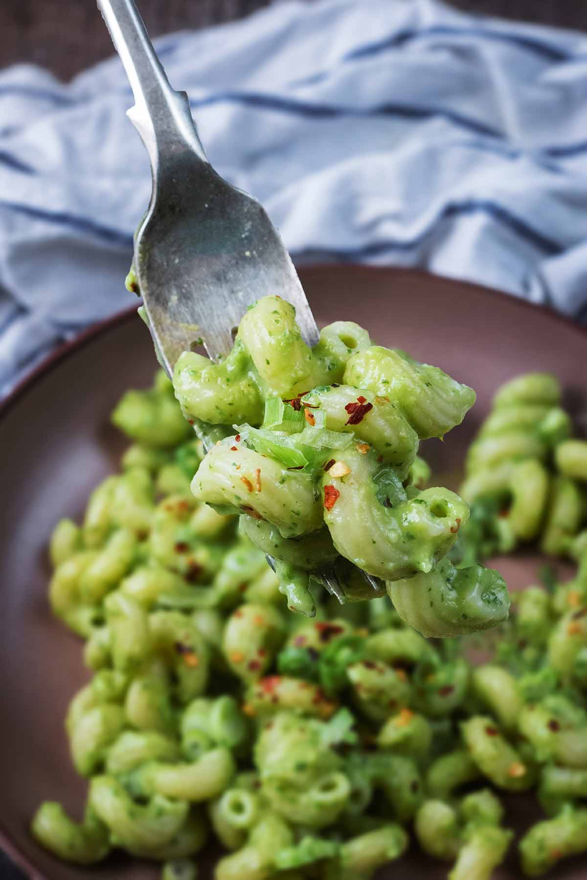 A fork lifting some avocado pasta fro a bowl.