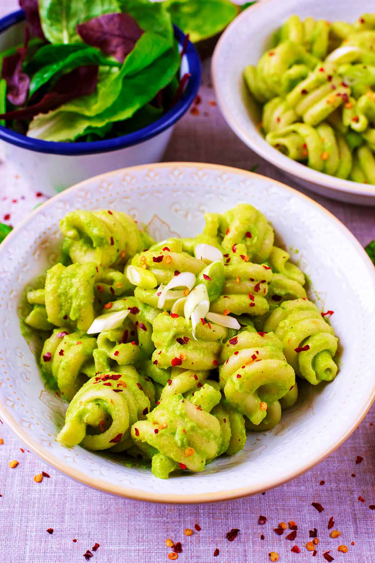 Avocado pasta in two bowls next to a side salad.