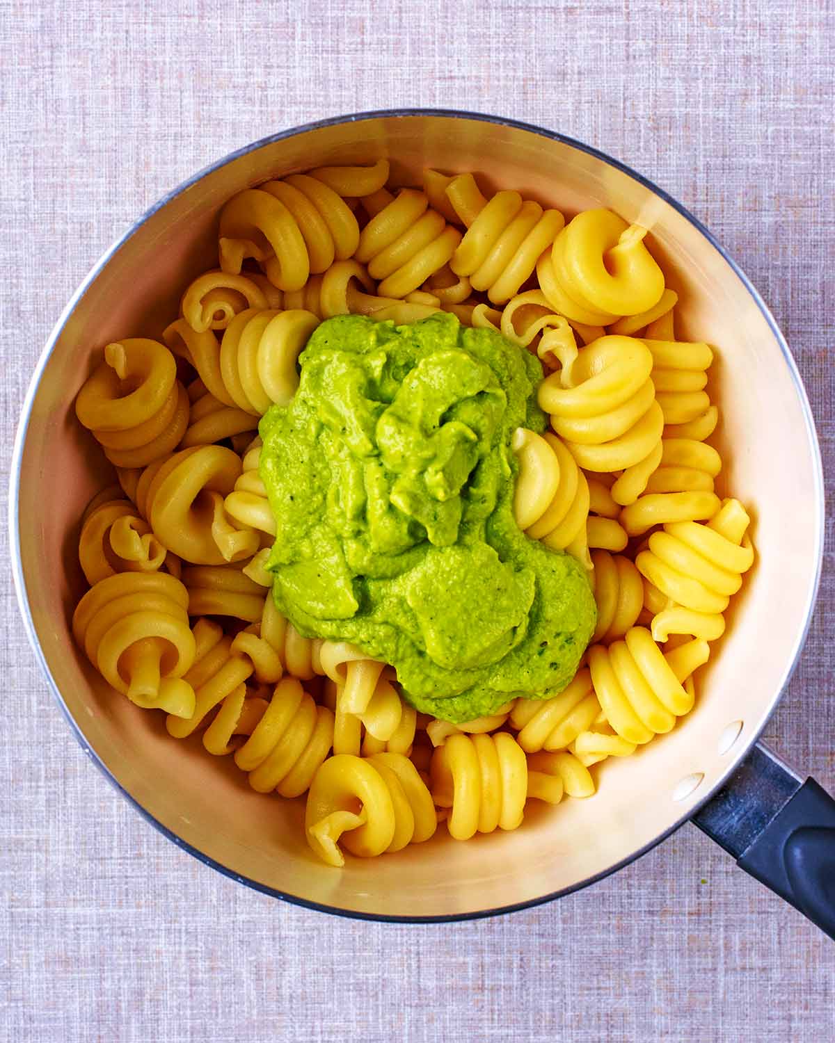 A saucepan of cooked pasta spirals with a large dollop of green sauce.