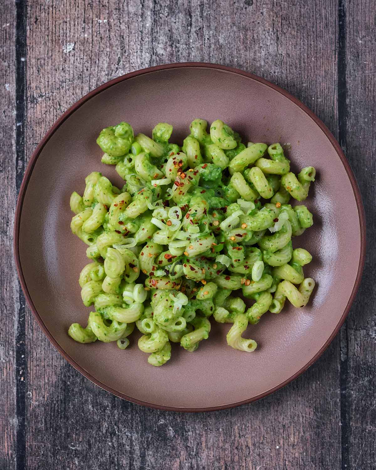 The avocado pasta on a plate topped with sliced spring onions and chilli flakes.