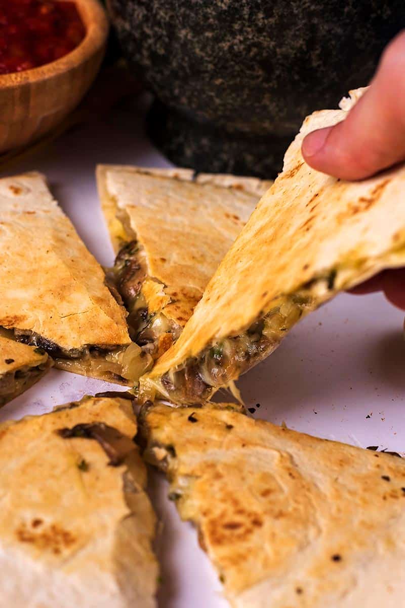 A quesadilla cut into slices with one slice being picked up.
