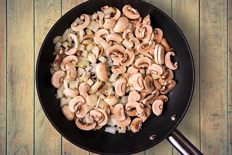 A frying pan with chopped onions and sliced mushrooms cooking in it.