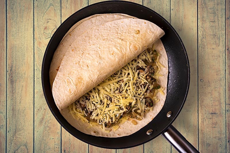 A frying pan with a mushroom quesadilla cooking in it.