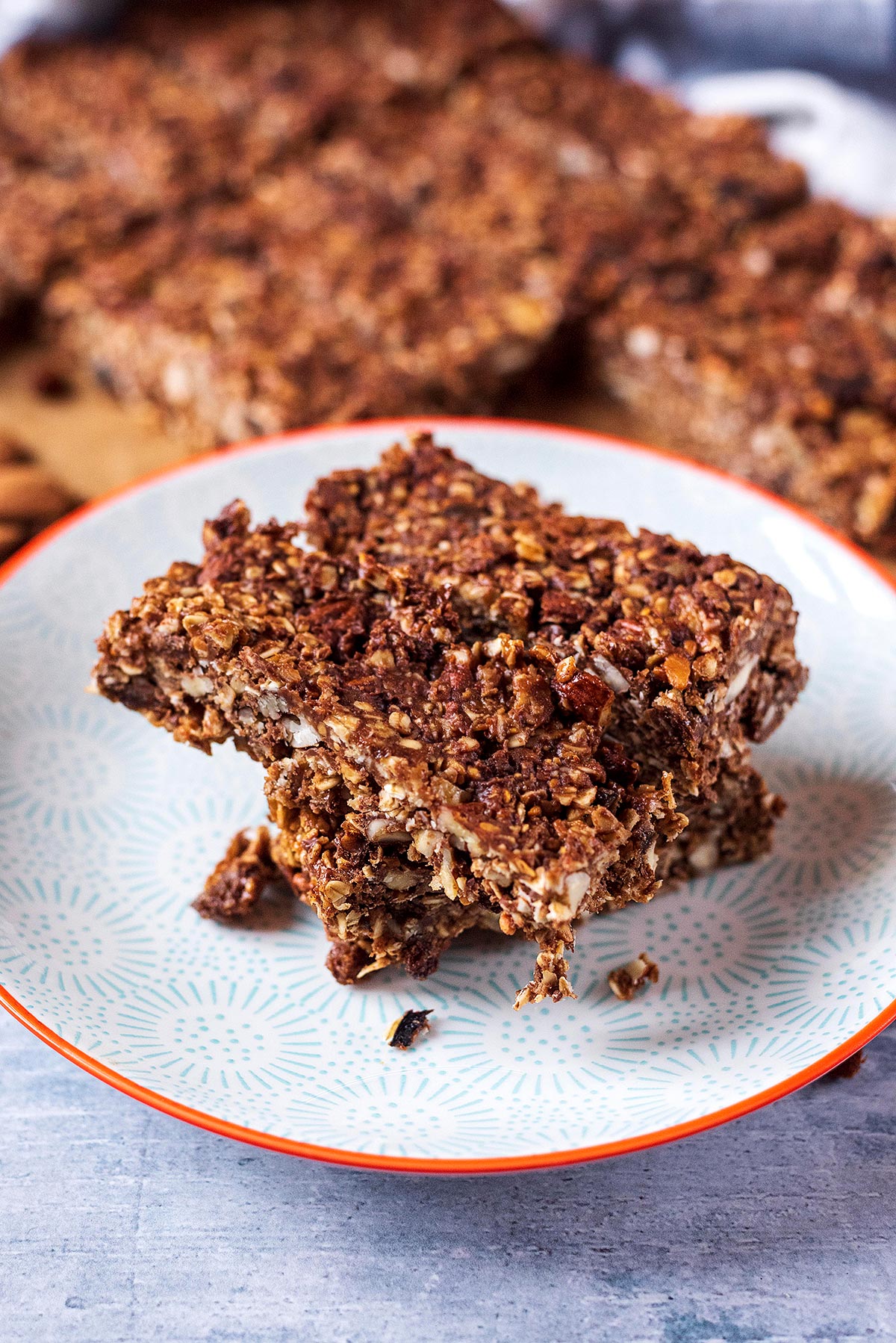 Granola bars on a plate with more bars in the background.