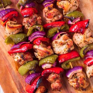 Four marinated chicken skewers on a wooden board.